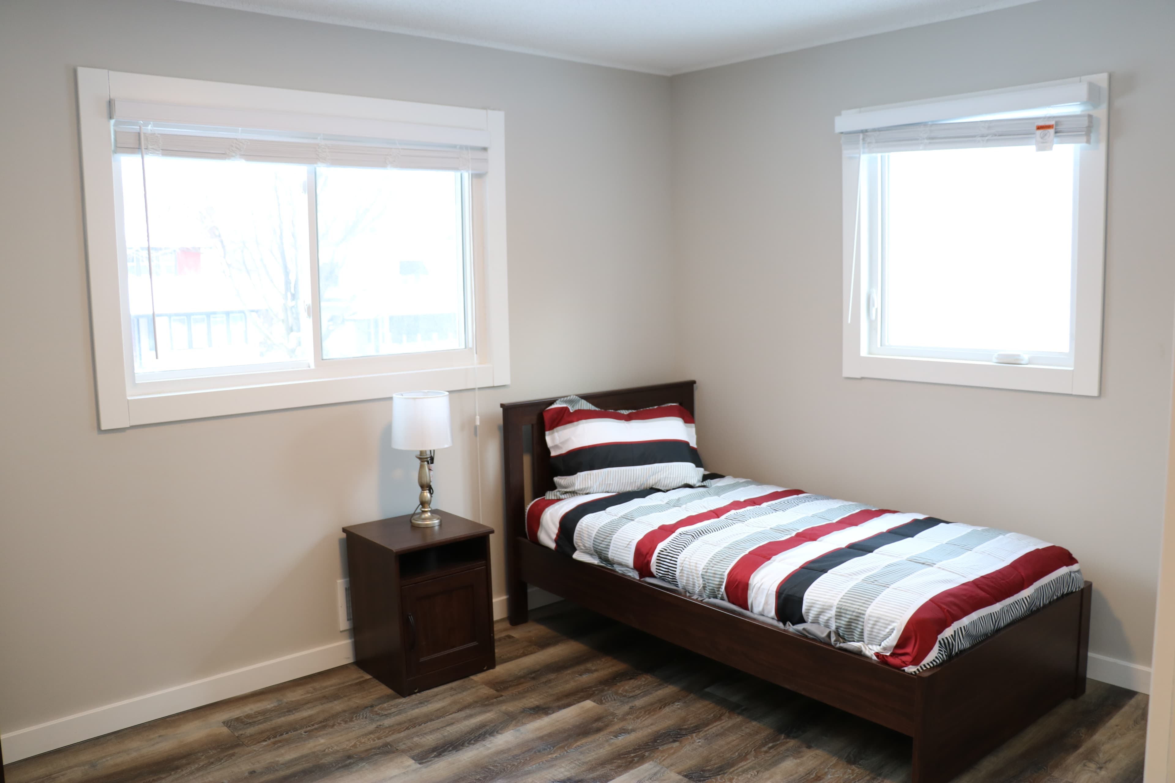 Private bedroom with a bed, nightstand, lamp, and natural light